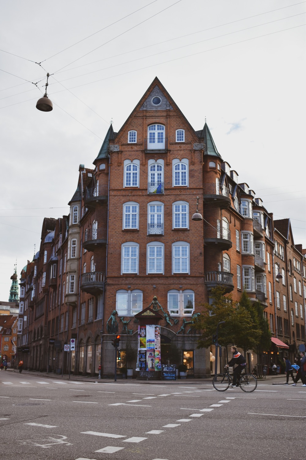 A cyclist crossing in front of a red brick Copenhagen building