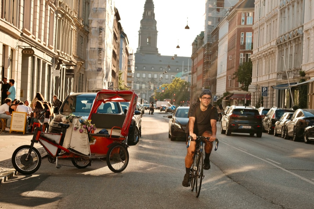 A flower-filled cargo trike with Christiansborg tower behind